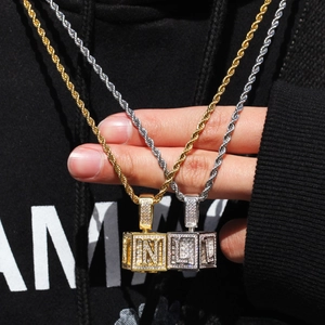 Vue macro de pendentifs cube hip-hop sertis de zircons et détail de la lettre N gravée
