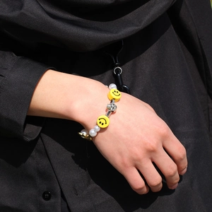 Detail of hip hop bracelet featuring pearls, yellow smiley faces and silver skull charms