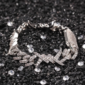 Detail of silver Cuban link bracelet with clear zircons and cross element on dark stone