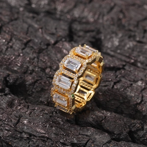 Macro shot of gold eternity ring with emerald cut stones and diamond halo on black rock