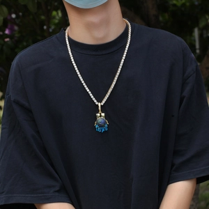 Hip hop tennis chain with a gold palm globe pendant on a male model in daylight