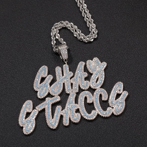 Close-up of iced out double layered GHA STACCS letter pendant with blue zircons