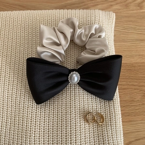Detail of satin bow hair clip with pearl embellishment and champagne scrunchie on knit fabric