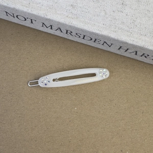Détail d'une barrette ovale en acétate crème avec strass irisés et fermoir en métal argenté