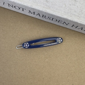 Détail d'une barrette en acétate bleu foncé ornée de strass et d'une écriture dorée
