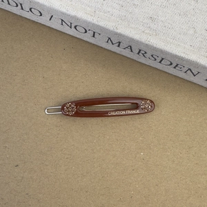 Gros plan sur la barrette en acétate marron avec strass et lettrage Creation France