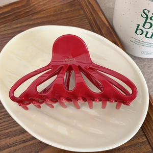 Detail of red glossy acetate hair claw with gold France Handmade logo on ceramic plate
