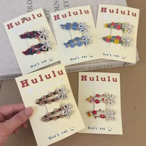 Floral embroidery hair clips with pearl beads on display card against a book background