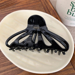 Detail of black glossy hair claw clip featuring gold France Handmade logo on a ceramic tray
