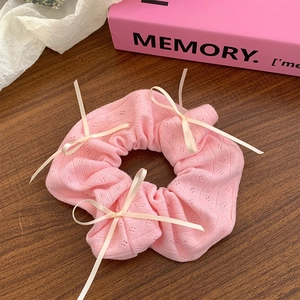 Pink knit scrunchie with beige ribbon bows on a wooden surface with a soft pink background