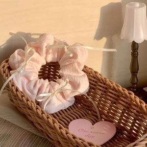 Detail of light pink knitted scrunchie with lace patterns and white ribbon bows