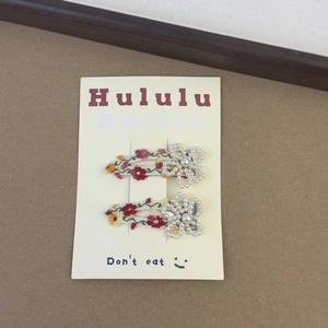 Detailed close-up of floral embroidery hair clips with white pearls on a display card