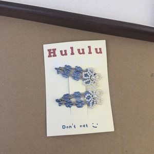 Detail of blue floral embroidery hair clips with pearls on a cardboard display card