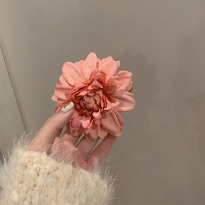 Close-up of a pink camellia flower hair clip with layered petals held in hand