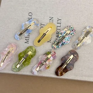 Eight colorful irregular wavy cellulose acetate hair clips with marble patterns on a book