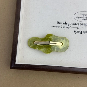 Detail of a wavy green marble acetate hair clip with a gold metal duckbill fastener