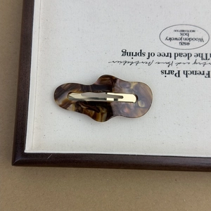 Detail of tortoiseshell acetate snap clip with irregular wavy edges and gold base
