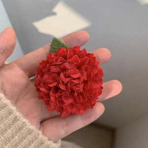 Gros plan d'une pince à cheveux fleur rouge en tissu avec détail de feuille verte