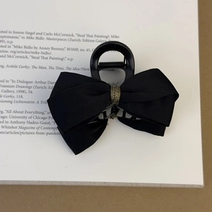 Détail d'une pince à cheveux à nœud en satin noir posée sur un magazine de mode chic