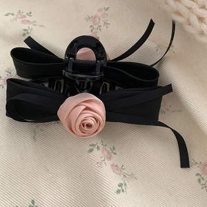 Detail of elegant black satin bow hair claw clip with a delicate pink fabric rose