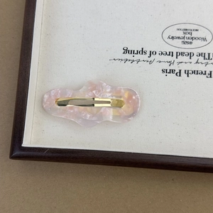 Close-up of pink marbled acetate cloud hair clip with golden alloy base on a display tray