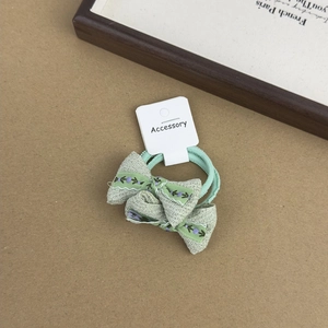 Detailed macro view of a light green floral embroidered bow hair tie with accessory tag