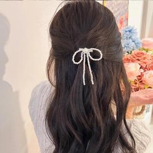 Elegant pearl bow hair clip with flowing tassels worn by a model in a sweet hairstyle