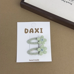 Detailed view of floral hair clips with green fabric petals and white beads on card