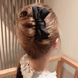 Detail shot of a large black fabric bow hair clip on a low bun in an elegant interior setting