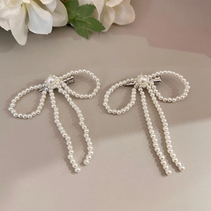 Detailed macro view of white pearl bow hair clips with elegant long tassels and silver clips