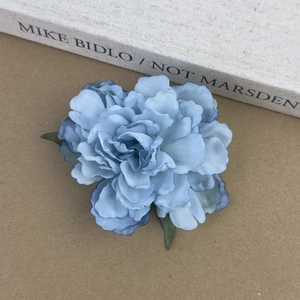 Détail d'une pince à cheveux fleur bleue artificielle multicouche avec feuilles vertes réalistes