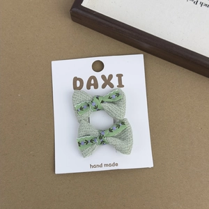 Close-up of light green knitted hair clips with purple flower embroidery on display card