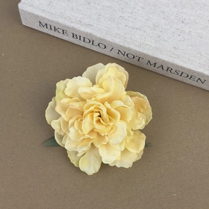 Détail macro d'une pince à cheveux pivoine jaune tendre avec feuille verte sur un livre
