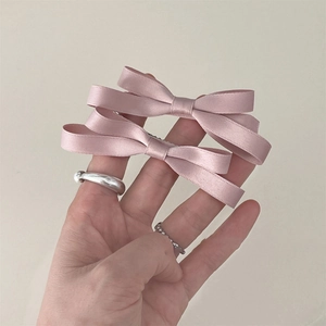 Close-up of a pair of light pink satin bow hair clips held in hand for a delicate look
