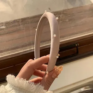 Detail eines eleganten, staubrosa Polsterhaarreifens mit Perlen und feiner Stoffstruktur