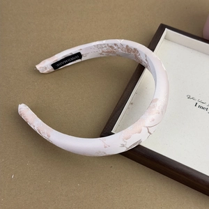 Close-up of a handmade jacquard satin headband featuring a delicate floral pattern tag