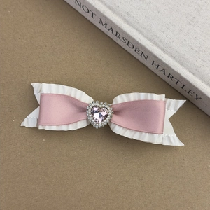 Detailed close-up of pink satin bow hair clip with lace trim and heart rhinestone