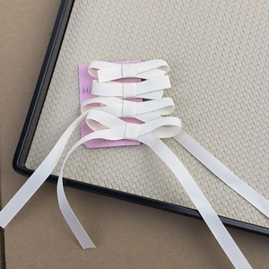 Detail view of four white ribbon bow hair clips on pink card in a beige woven tray