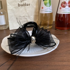 Dettaglio della molletta per capelli con fiocco in pizzo nero, piume e strass chic