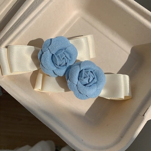 Set of two light blue fabric camellia and satin bow hair clips for women on a tray