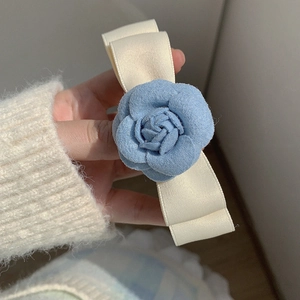 Detailed shot of a blue camellia fabric flower hair clip with a cream ribbon bow design