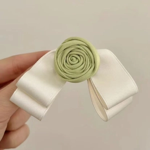 Detailed close-up of a handmade rose bow hair clip with light green fabric and white silk