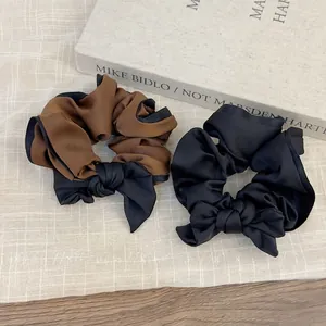 Brown and black satin bow scrunchies displayed on a warm beige checkered background