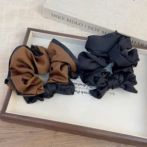 Brown and black oversized bow hair scrunchies with satin sheen in a wooden tray