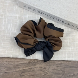 Close-up of a brown and black bow hair scrunchie with piping on a rustic wooden desk
