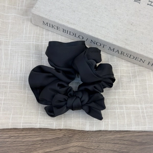Close-up of black satin scrunchie with bow detail on a minimalist wooden background