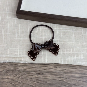 Detail of a dark brown hollow bow hair tie with glossy resin finish on soft linen fabric