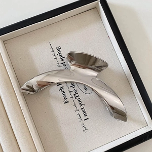 Close-up of a silver arched metal hair claw clip with a polished mirror finish on a tray