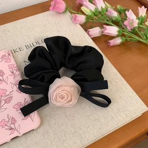 Chouchou français avec rose en maille et nœud noir posé sur un livre crème