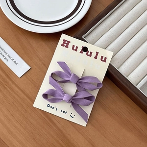 Dettaglio di due fermagli per capelli a fiocco in tessuto viola su scheda del marchio